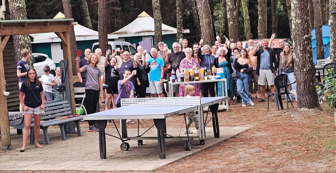 Les campeurs du Gaoucher réunis sous les pins, verre levé, autour de la table de ping-pong